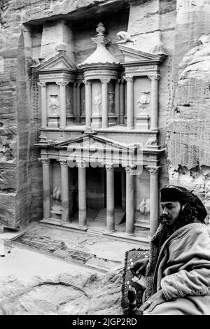 Ein lokaler Beduinenmensch in typischer Kleidung mit dem Äußeren des Schatzhauses ‘Al-Khazneh’ im Hintergrund, Petra, Jordanien. Stockfoto