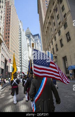 Am Unabhängigkeitstag, dem 4.. Juli, marschieren Männer mit amerikanischen Flaggen in Revolutionary war Uniformen auf der Broad Street im historischen Finanzdistrikt von Lower Manhattan hinauf. Stockfoto