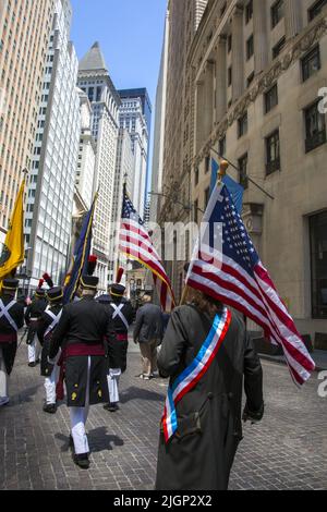 Am Unabhängigkeitstag, dem 4.. Juli, marschieren Männer mit amerikanischen Flaggen in Revolutionary war Uniformen auf der Broad Street im historischen Finanzdistrikt von Lower Manhattan hinauf. Stockfoto