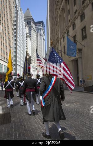 Am Unabhängigkeitstag, dem 4.. Juli, marschieren Männer mit amerikanischen Flaggen in Revolutionary war Uniformen auf der Broad Street im historischen Finanzdistrikt von Lower Manhattan hinauf. Stockfoto
