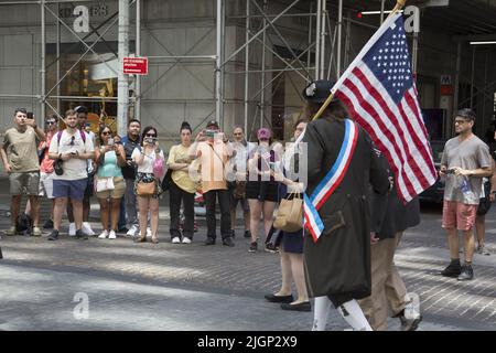Am Unabhängigkeitstag, dem 4.. Juli, marschieren Männer mit amerikanischen Flaggen in Revolutionary war Uniformen auf der Broad Street im historischen Finanzdistrikt von Lower Manhattan hinauf. Stockfoto
