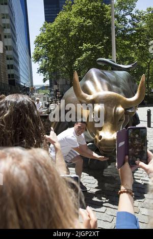 Touristen stehen an, um ihre Fotos mit dem berühmten Wall Street Bull am unteren Broadway in Manhattan, New York City, zu machen. Stockfoto