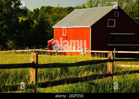 Eine rote Scheune steht hinter einem gespaltenen Eisenbahnzaun, der ein Farmfeld in der ländlichen Gegend des Hudson River Valley in der Nähe von New Paltz umgibt