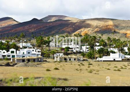 Traditionelle Architektur von Lanzarote, Kanarische Inseln: Weiße zweistöckige Häuser vor einem bunten Hügel aus verwittertem vulkanischem Material. Stockfoto