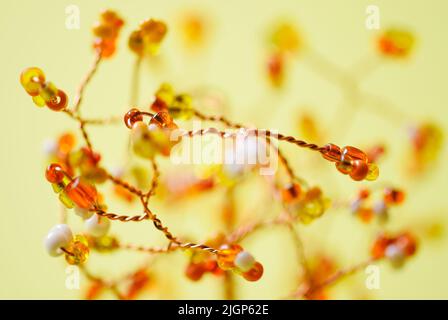 Glänzende Perlen in orange weiß mit geflochtenem Kupferdraht. Gelber heller Hintergrund. Nahaufnahme. Abstraktes Muster, Tapete Stockfoto