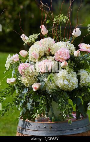 Blumenarrangement zur Hochzeit mit Hortensien, Pfingstrosen und Rosen. Blumen stehen auf einem großen Fass draußen. Stockfoto