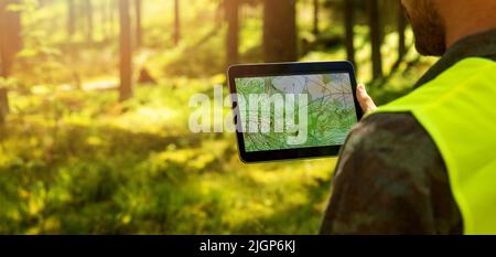 Mann, der mit topografischen Kartendaten auf einem digitalen Tablet im Wald arbeitet. Banner mit Kopierraum Stockfoto