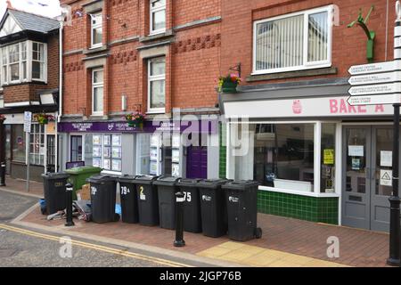 Holywell, Großbritannien: 19. Jun 2022: Eine Gruppe von Mülltonnen steht auf dem Bürgersteig auf der High Street vor Geschäften. Stockfoto