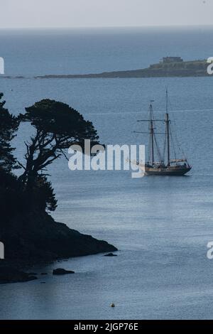 Ein klassisches Segelboot segelt in glitzerndem Wasser in Richtung Cow's Beach und dem offenen Meer von Durgan auf dem Helford River in Cornwall. Stockfoto