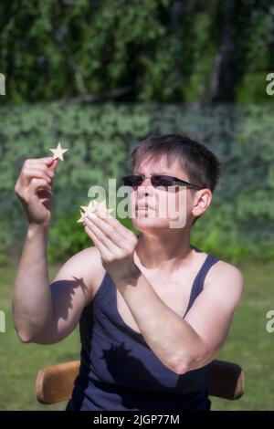 Frau, die im Sommer im Garten sitzt und kleine Holzsterne hält, Übersichtskonzept. Stockfoto