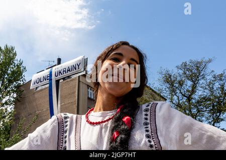 Krakau, Polen. 12.. Juli 2022. Ukrainische Frau posiert unter dem Schild „Independent Ukraine Square“ während einer Zeremonie, die einem Platz in der Altstadt von Krakau den Namen „Independent Ukraine“ verleiht. Die lokale Regierung betont, dass sie die Entscheidung getroffen hat, Unterstützung und Einheit mit dem ukrainischen Volk zu zeigen. Der Ort für den ukrainischen Unabhängigkeitsplatz wurde bewusst in unmittelbarer Nähe des russischen Konsulats in Krakau gewählt. Kredit: SOPA Images Limited/Alamy Live Nachrichten Stockfoto