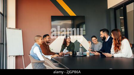 Glückliche Geschäftsleute, die sich in einem Sitzungssaal treffen. Gruppe von multiethnischen Geschäftsleuten, die während ihrer morgendlichen Unterweisung fröhlich lächeln. Junge Entr Stockfoto