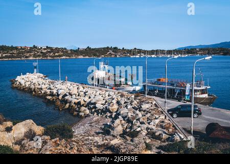 Ein Fischerboot und ein für Touristen anlegtes Kreuzschiff sind am Pier vertäut. Ormos Panagias auf der Halbinsel Sithonia in Chalcidice, Griechenland Stockfoto