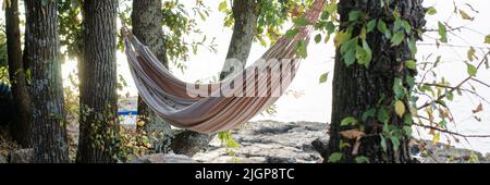 Leere Hängematte, die zwischen Bäumen im Schatten am Strand gebunden ist. Stockfoto