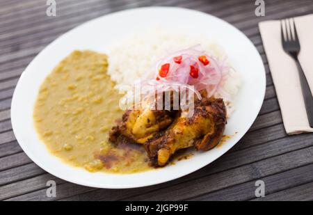 Hähnchenflügel mit pürierten Erbsen, Reis und eingelegten Zwiebeln auf weißem Teller Stockfoto