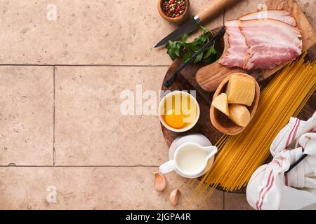 Zutaten für Pasta Carbonara. Traditionelle italienische Pasta Carbonara Zutaten Speck, Spaghetti, Parmesan und Eigelb, Knoblauch. Beigefarbener Tisch mit alten Fliesen Stockfoto