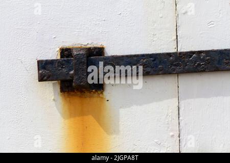 Texturen und rostige, schuppige Farbe und korrodierte Metallteile an der hölzernen Strandhütten-Tür. Rostiger Fleck auf der alten weißen Farbe von der rostigen Sicherheitsstange und dem Haken Stockfoto