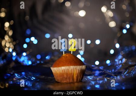 Leckerer Vanillekuchen oder Muffin mit der Nummer 12 zwölf auf Alufolie und unscharfem hellen Hintergrund. Digitales Grußkartenkonzept für Urlaub oder Geburtstag. Hochwertige Fotos Stockfoto