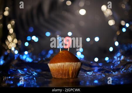 Digitales Grußkartenkonzept für Urlaub oder Geburtstag. Leckerer Vanillekuchen oder Muffin mit der Nummer 19 19 auf Aluminiumfolie und unscharfem, hellem Hintergrund. Hochwertige Fotos Stockfoto