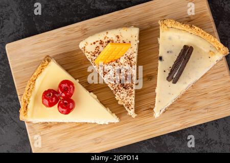 Klassischer Käsekuchen mit Kirschen, Schokolade und Keksen auf einem Tablett auf dunklem Hintergrund Stockfoto