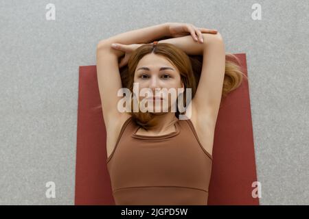 Schlanke junge Frau, die in Supta Virasana liegt, in der Liegenden Heldenpose, die Bauch- und Rückenmuskulatur im Fitnessstudio auf der Matte dehnt Stockfoto