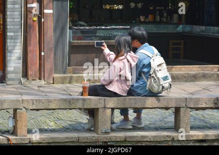 Ein junges Paar, das zusammen ein Selfie machen, saß an einem Kanalufer in der chinesischen Stadt Suzhou. Stockfoto