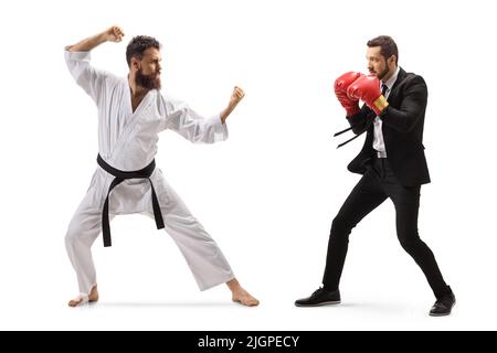 Ganzkörperaufnahme eines Geschäftsmannes mit Boxhandschuhen, der mit einem Mann im Karate-Kimono auf weißem Hintergrund kämpft Stockfoto