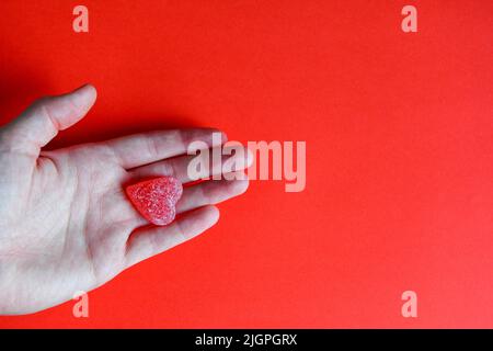 Foto von roten Gelee Süßigkeiten Herz in der Hand der Frau auf rotem Hintergrund Stockfoto