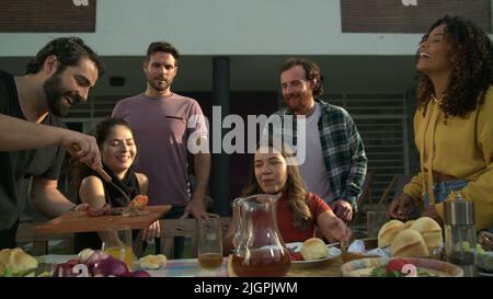 Barbecue Chef bringt Essen zu Freunden vereint um den Tisch im Hinterhof zu Hause Stockfoto