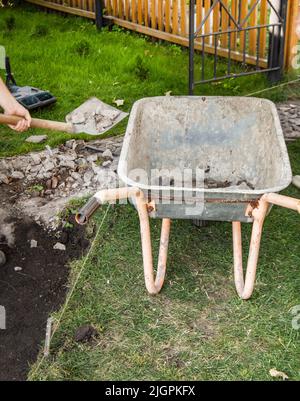 Eine leere alte rostige Schubkarre für die Entfernung von Erde während des Baus eines neuen Gartenweges, im Freien, im Sommer, Hinterhof. Stockfoto