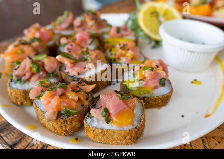 Sushi-Rollteller mit Lachs und Sauce darauf. Traditionelles japanisches Essen im mexikanischen Stil Stockfoto