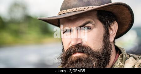 Ledermütze Mit Cowboy-Design. Porträt eines jungen Mannes mit Cowboyhut. Cowboys im Hut. Schöner bärtiger Macho. Mann unrasiert Cowboys. Amerikanischer Cowboy Stockfoto