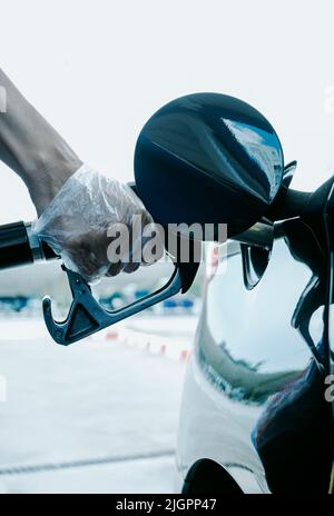 Ein junger Kaukasusmann, der Plastikhandschuhe trägt, füllt den Kraftstofftank des Autos in einer Tankstelle Stockfoto