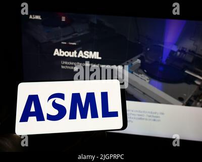 Person mit Mobiltelefon und Logo des niederländischen Halbleiterunternehmens ASML Holding NV auf dem Bildschirm vor der Business-Webseite. Konzentrieren Sie sich auf die Telefonanzeige. Stockfoto