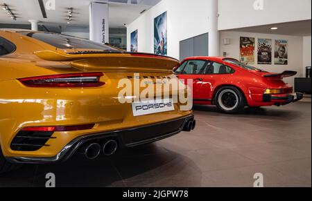 Ein Bild eines orangefarbenen Porsche 911 Turbo S neben einem roten Porsche 911 Carrera 3,0 im Autohaus. Stockfoto