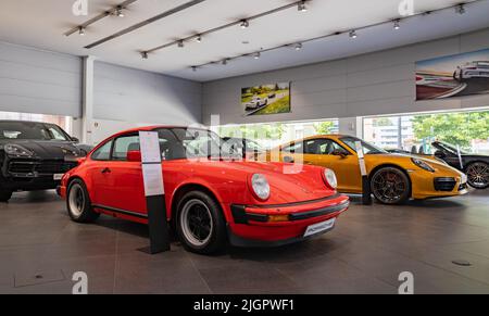 Ein Bild eines roten Porsche 911 Carrera 3,0 neben einem orangefarbenen Porsche 911 Turbo S im Autohaus. Stockfoto