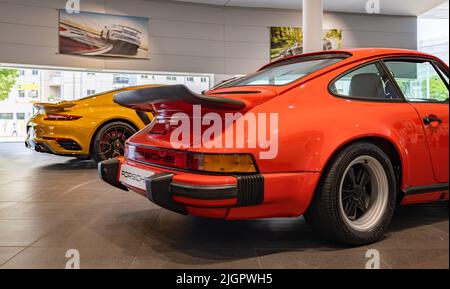 Ein Bild eines roten Porsche 911 Carrera 3,0 neben einem orangefarbenen Porsche 911 Turbo S im Autohaus. Stockfoto