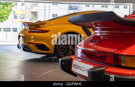 Ein Bild eines roten Porsche 911 Carrera 3,0 neben einem orangefarbenen Porsche 911 Turbo S im Autohaus. Stockfoto