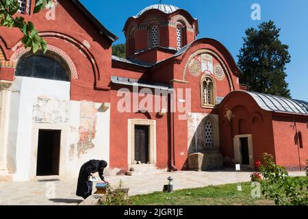 Eine schwarze Mönchin, die vor dem mittelalterlichen serbisch-orthodoxen Kloster „Patriarchat von Peć“ im Kosovo Kleidung bügelt. Stockfoto