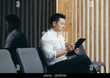 Asiatischer Mitarbeiter im Wartezimmer füllt Fragebogen aus, Geschäftsmann bekommt einen Job in einem modernen Büro. Stockfoto