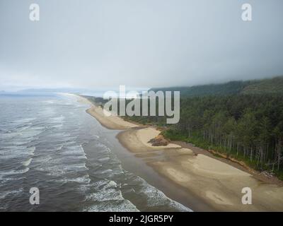 Seascape. An einem langen Sandstrand laufen helle weiße Wellen, Wellen auf dem Wasser. Ein Kiefernwald wächst auf einem Hügel in der Nähe des Ufers. Menschenleeres Hotel. Die Schönheit Stockfoto