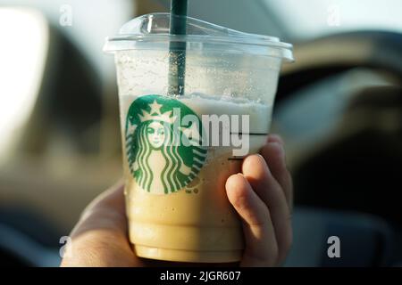 Eine Person, die eine Starbucks Kaffeetasse im Auto hält. Stockfoto