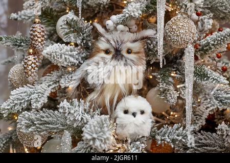 Weihnachtsspielzeug in Form einer Eule und ihres kleinen Jungen auf einem geschmückten Weihnachtsbaum. Stockfoto