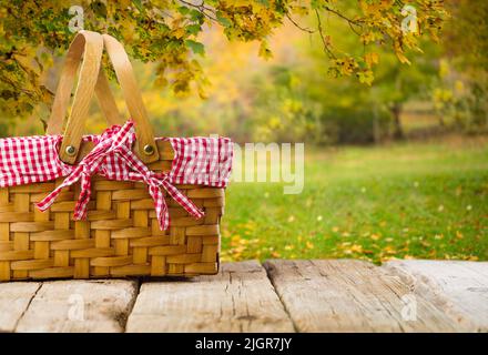 Erntedankfest, Erntetag in der Natur. Auf einem Holztisch, ein niedlicher Picknickkorb vor dem Hintergrund der luxuriösen Herbstnatur, golden l Stockfoto