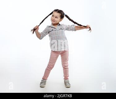 Charmantes kleines Mädchen mit geflochtenen Zöpfen im Studio auf weißem Hintergrund. Stockfoto