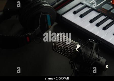 Professionelle Studioausstattung - Mikrofon, Kopfhörer und Midi-Tastatur auf grauem Hintergrund. Tonstudio, Musikstudio, Arbeitsplatz eines Musikers Stockfoto