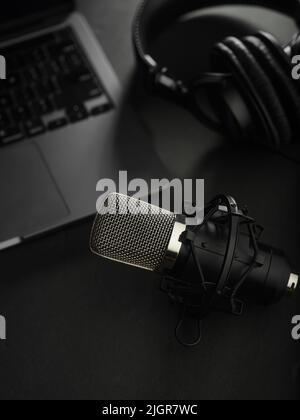 Heimbüro. Studio-Mikrofon, Kopfhörer und Laptop auf grauem Hintergrund. Journalismus, Radio, Blogging, Präsentationen, Software, Audio, Podcast. Bann Stockfoto