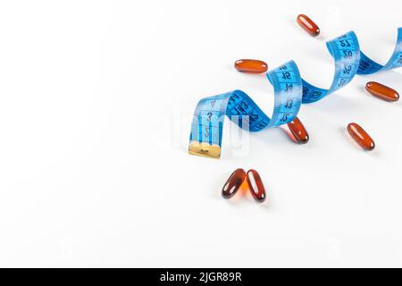 Stapel von Leptin-Kapseln mit blauem Maßband auf weißem Hintergrund. Konzept der Gewichtsabnahme, Ernährung, Fettverbrennung, gesunde Ernährung. Speicherplatz kopieren. Stockfoto