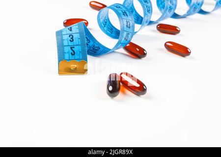 Stapel von Leptin-Kapseln mit blauem Maßband auf weißem Hintergrund. Konzept der Gewichtsabnahme, Ernährung, Fettverbrennung, gesunde Ernährung. Speicherplatz kopieren. Stockfoto