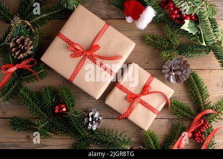 Weihnachts-Kraft-Geschenkbox mit rotem Band auf rustikalem Holzhintergrund, Weihnachtsgeschenk Hintergrund mit natürlichen Tannenzweigen, Zapfen, gemütliche Weihnachten s Stockfoto